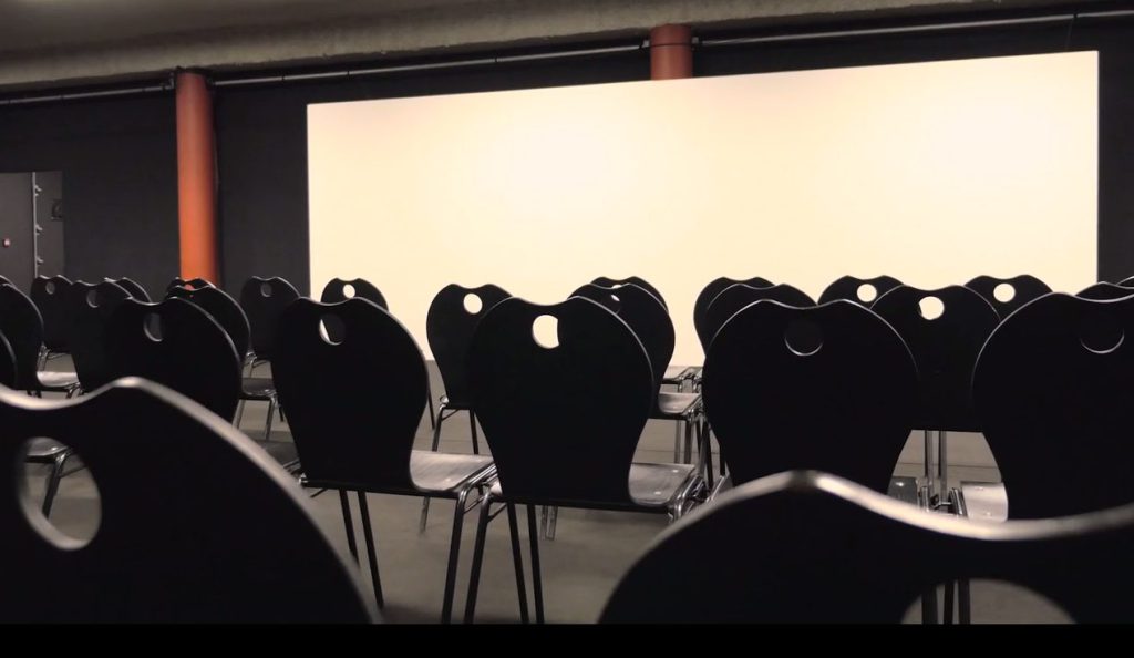 Rangées de chaises noires face à un grand écran blanc dans une salle de projection Espace Glenmor